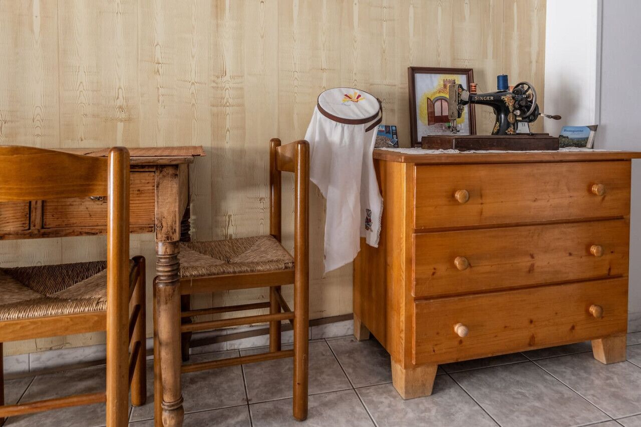 A wooden chair with a woven seat, a wooden dresser with drawers, and a vintage Singer sewing machine on a wooden table.