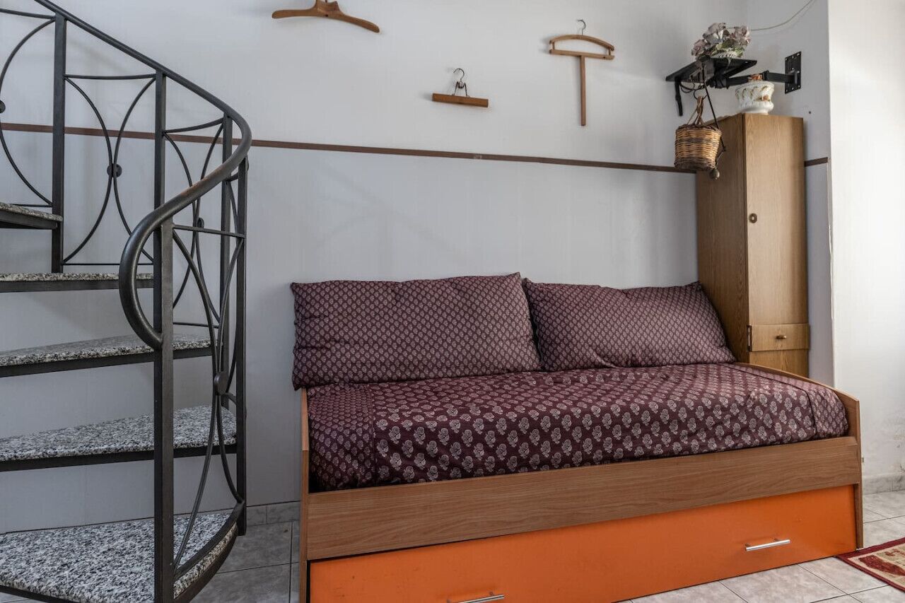 Une chambre à coucher comprenant un lit, une armoire en bois, un escalier en colimaçon en métal et une étagère fixée au mur.