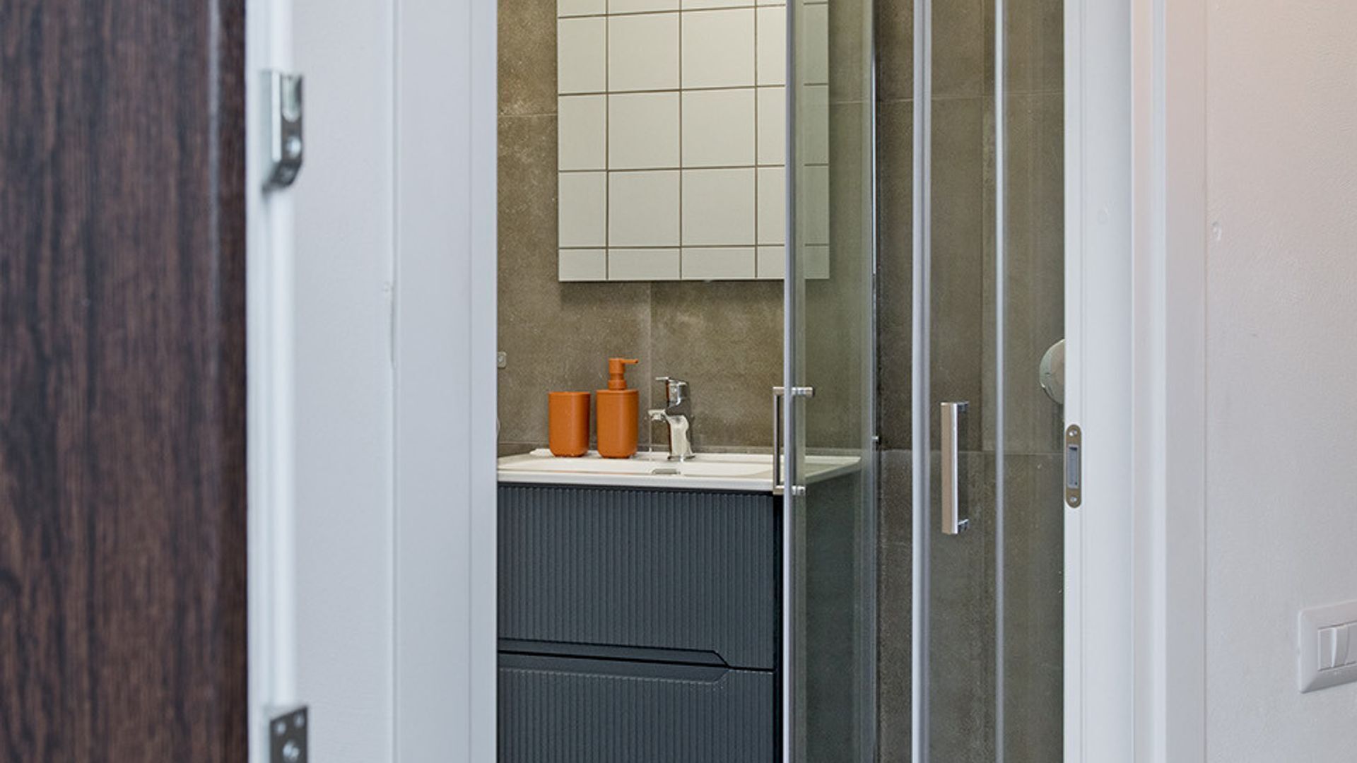 A bathroom with a glass shower door, a white sink, and a mirror above it.