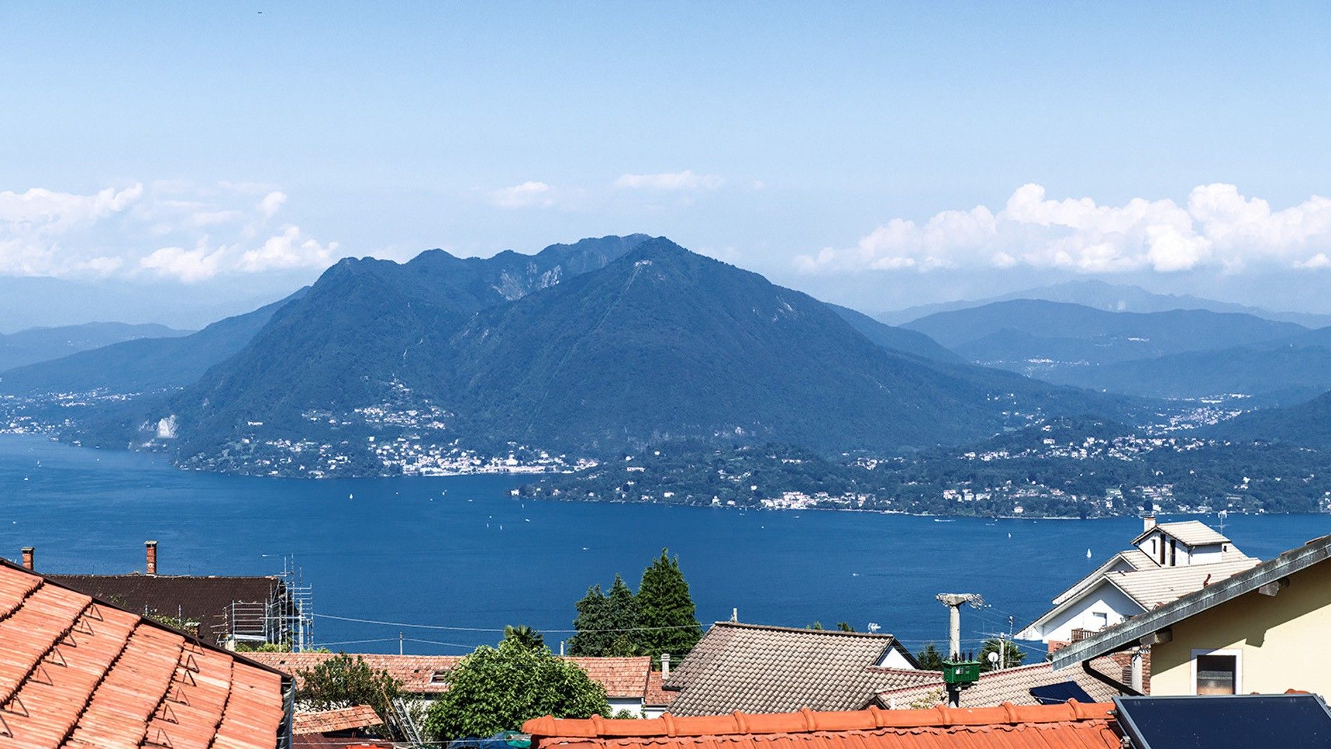 A mountain with a clear view of the sea and a town in the background.