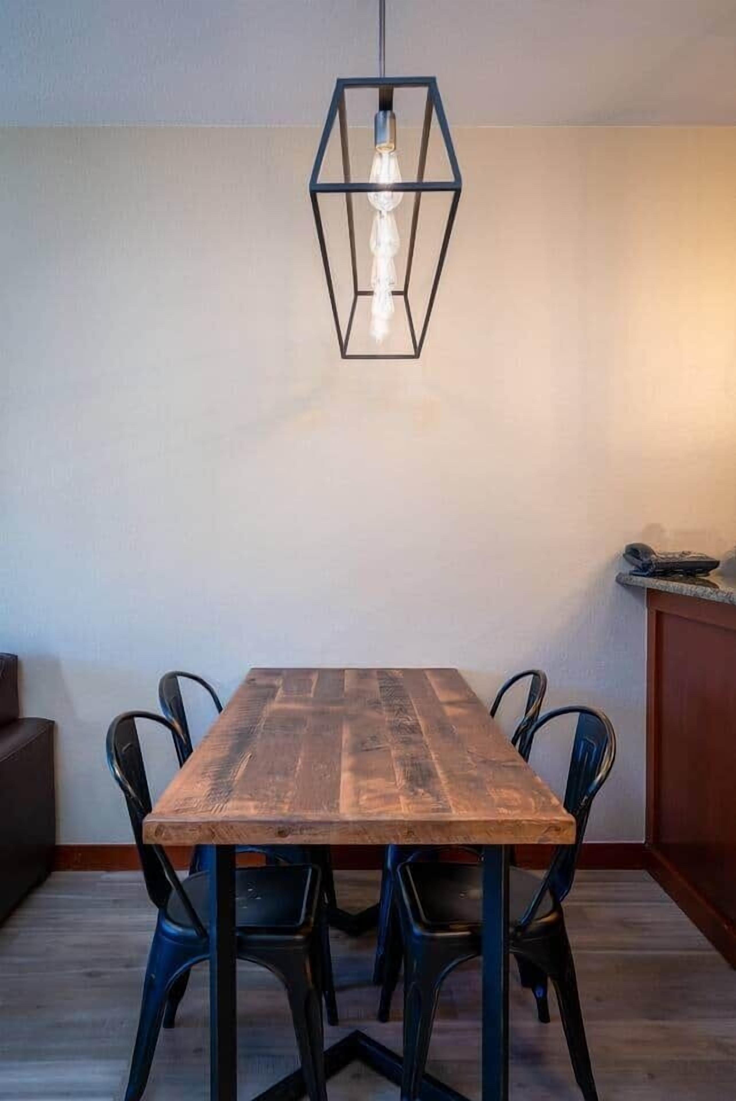 A dining area with a wooden table and black chairs, a hanging light fixture, and a kitchen counter in the background.