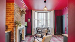 Une pièce avec une cheminée, un tapis à carreaux et un coin repas avec des chaises.