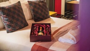 Une chambre d’hôtel avec un lit, des oreillers, une boîte de verres à vin et une serviette pliée.
