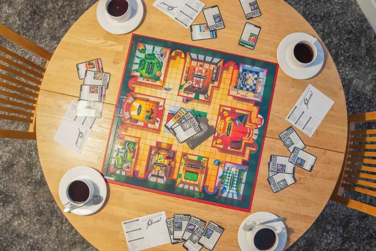 A board game with a colorful layout and cards, surrounded by cups of coffee on a round table.