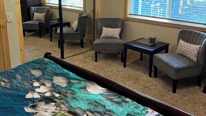 Una habitación con una cama, dos sillones, una mesita y un televisor. Cuenta con ventanas con persianas, piso alfombrado y techo de madera.