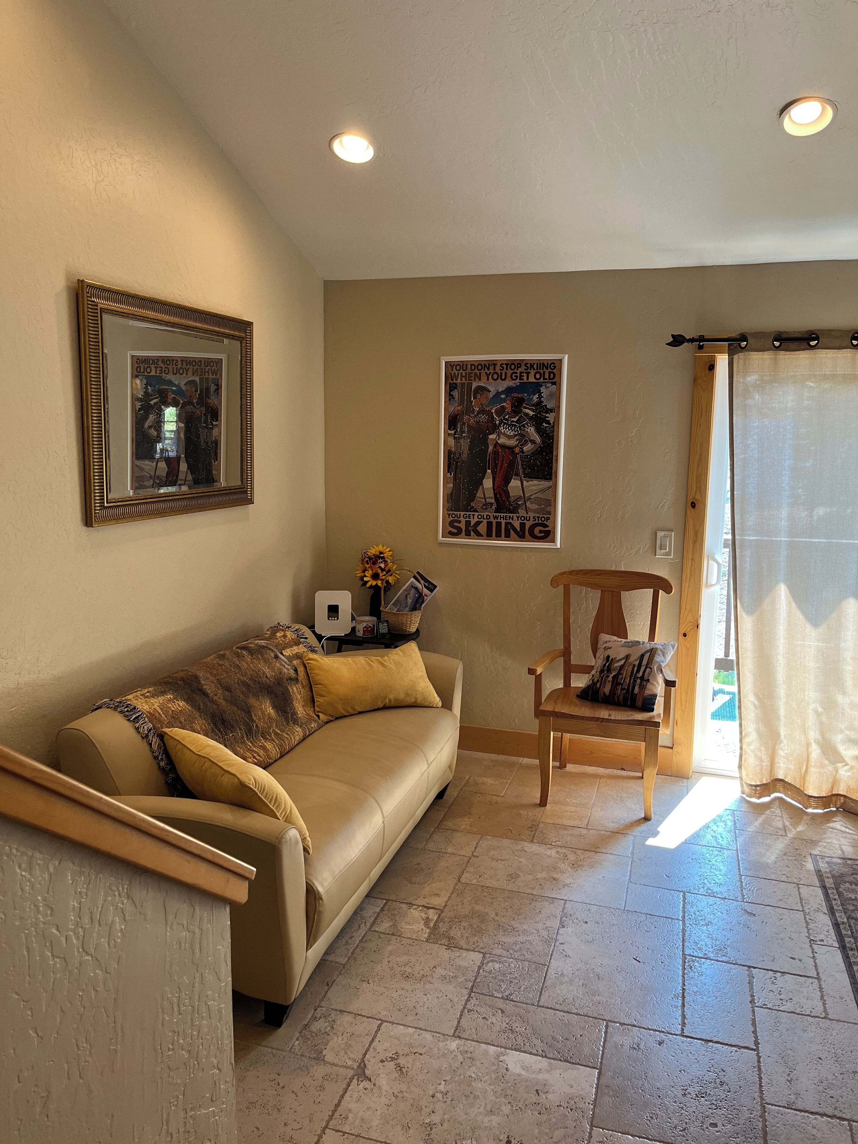 A living room with a sofa, a chair, a framed picture, a poster, and a window with curtains.