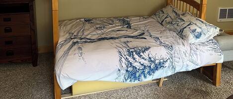 Un letto a castello con copriletto fantasia, una cassettiera in legno e un quadro appeso al muro.