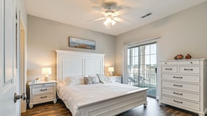 A bedroom with a large bed, a nightstand with a lamp, a dresser, and a window with a view. - Myrtle Beach / Surfside Beach Condo: 3 Mi to Ocean (Myrtle Beach)