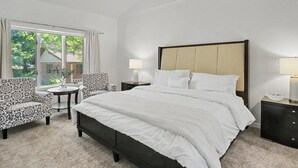 A hotel room with a large bed, two nightstands, a chair, a small table, and a window with curtains. - Spacious & Lovely 4-BR Home Minutes to WEC, HITS (Ocala)