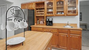 A kitchen with wooden cabinets, a stainless steel refrigerator, a coffee maker, and a hanging mug rack. - Spacious & Lovely 4-BR Home Minutes to WEC, HITS (Ocala)
