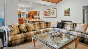 A living room with a checkered sofa, a glass coffee table, and a kitchen in the background. - Spacious & Lovely 4-BR Home Minutes to WEC, HITS (Ocala)