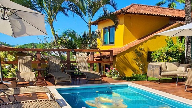 Un espace piscine avec des chaises longues, une piscine à l’eau d’un bleu limpide et un bâtiment jaune surmonté d’un toit en tuiles.
