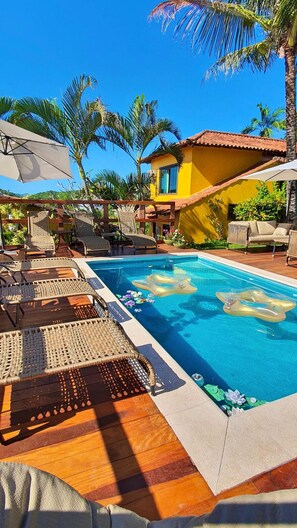 A pool area with lounge chairs, a clear blue pool, and a yellow building with a tiled roof. - Pousada Star Búzios  (Búzios)