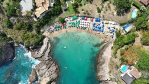 Vue aérienne d’une plage bordée d’une côte rocheuse, avec une zone de baignade, ainsi que plusieurs parasols et chaises longues.