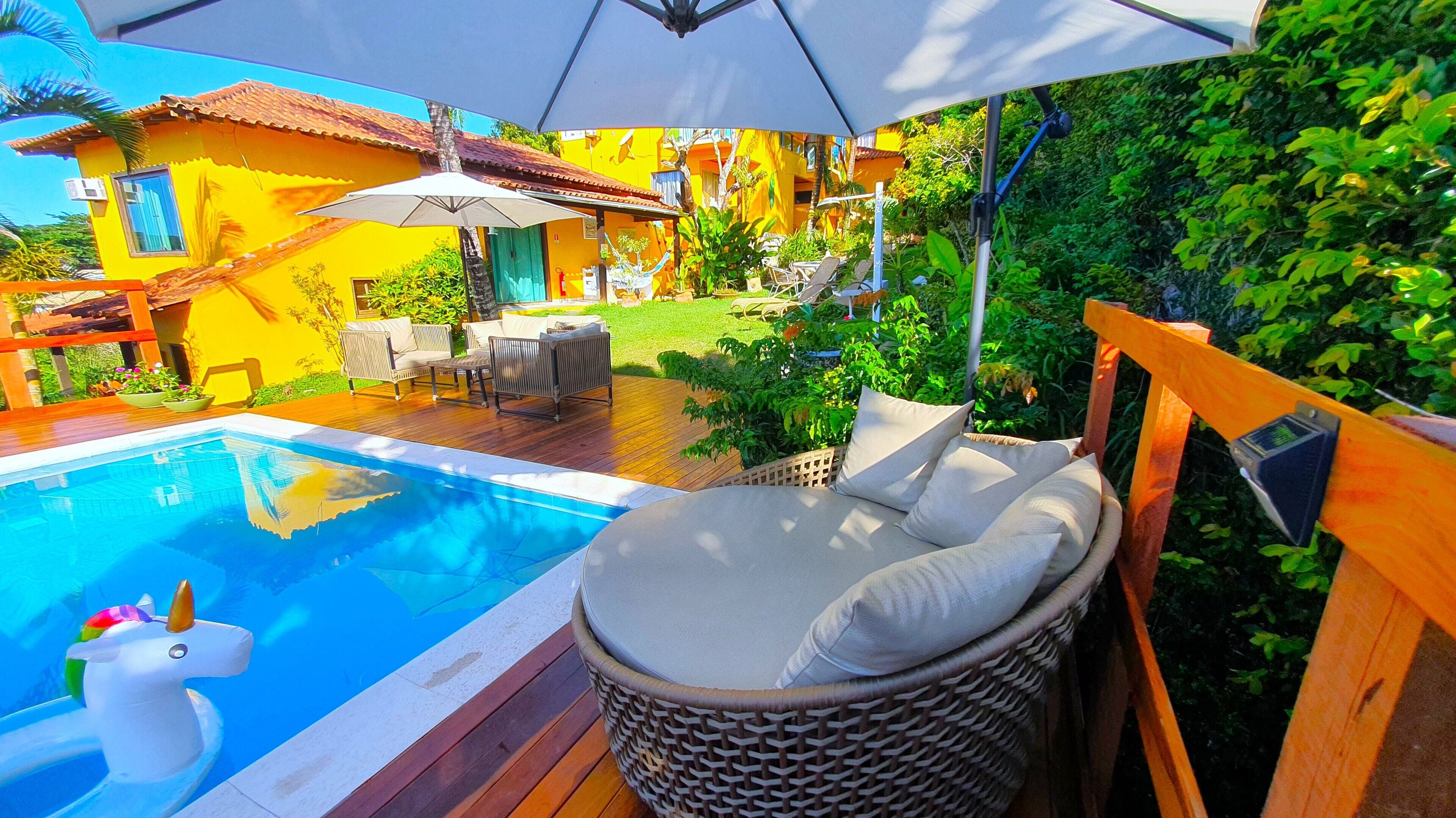 A pool area with a wicker chair and an umbrella, surrounded by a wooden deck and a small garden.