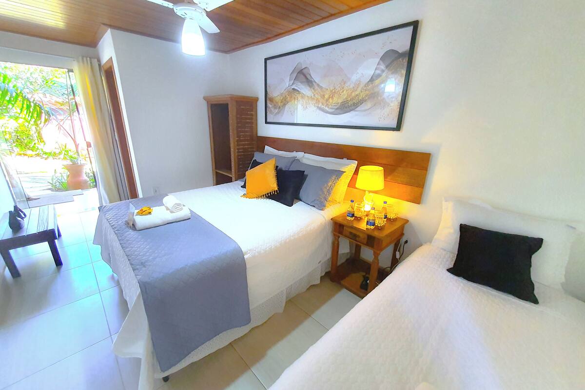 Quarto de hotel com cama, mesa de cabeceira com abajur, ventilador de teto e um quadro na parede.
