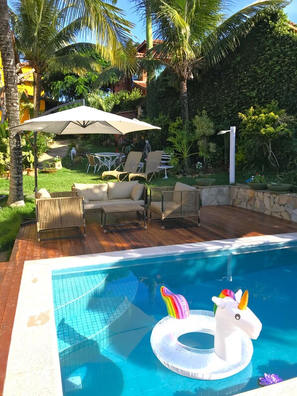 A swimming pool with a unicorn float, surrounded by lounge chairs and a covered patio area. - Pousada Star Búzios  (Búzios)