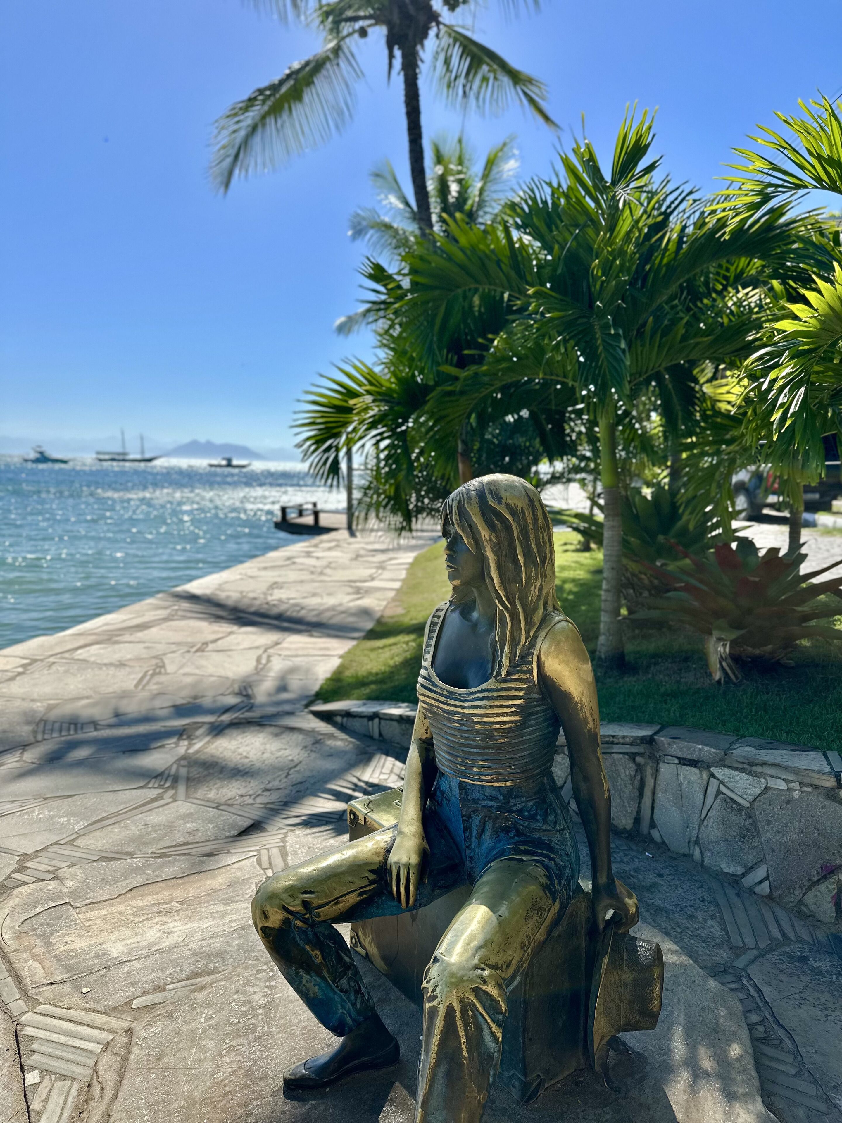 A bronze statue of a seated figure with a clear view of the ocean and palm trees in the background.