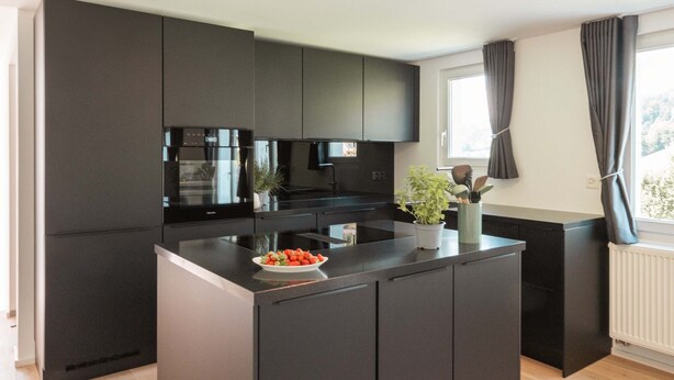 A modern kitchen with dark cabinetry, a central island, and a window with curtains.