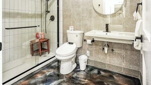 Un baño con ducha, inodoro, lavamanos y un taburete de madera pequeño.