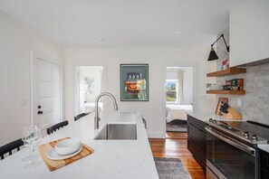 A modern kitchen with a white marble island, stainless steel appliances, and a black pendant light. - Urban Retreat: Bright, Stylish Top-Floor Apartment Near Universities & Dining (Providence)