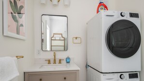Een moderne badkamer met een witte wastafel, gouden details, een spiegel en gestapelde wasmachines.