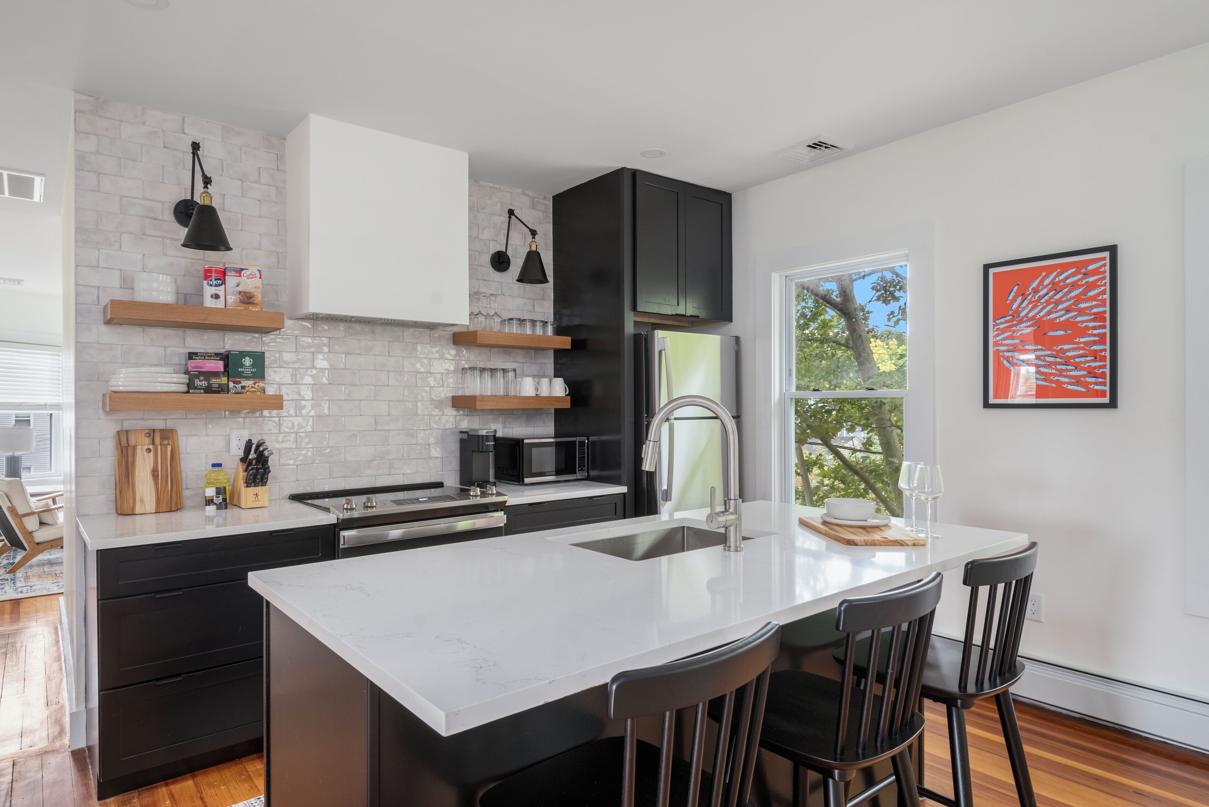 A modern kitchen with a white island, black cabinets, and a large window.