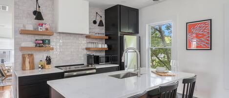 A modern kitchen with a white island, black cabinets, and a large window.