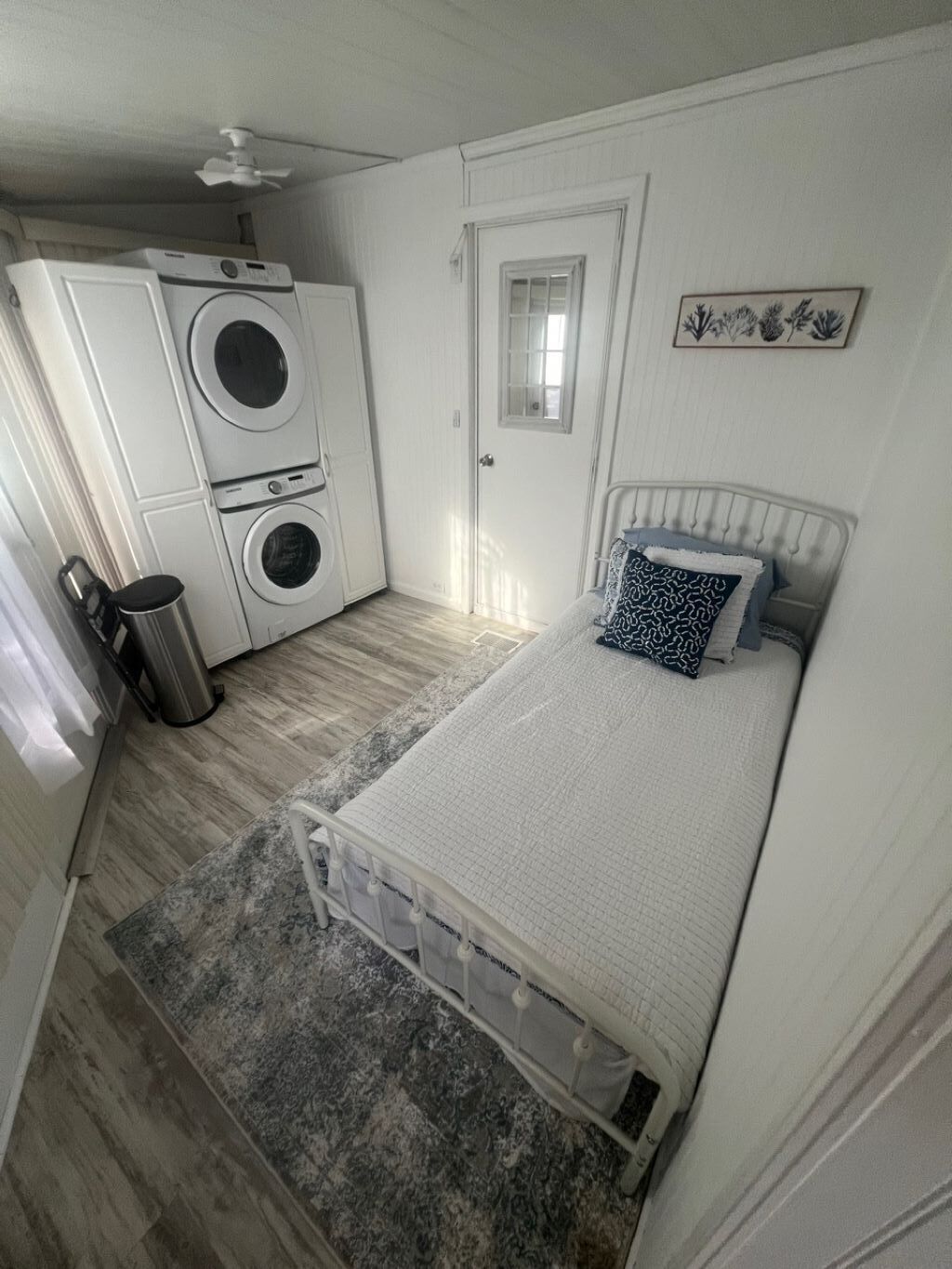 Une chambre avec un lit, un lave-linge, une petite fenêtre et une porte.