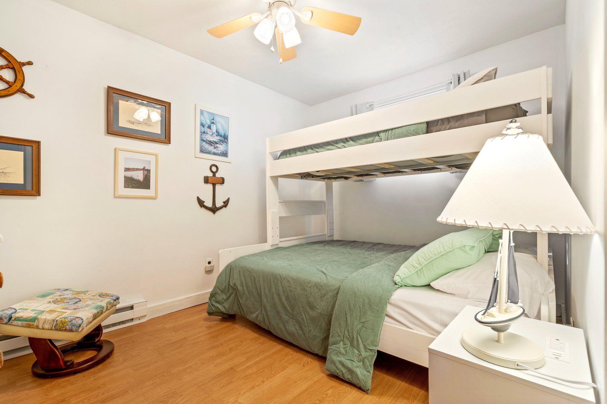 A bunk bed room with a ceiling fan, framed pictures on the wall, and a bedside lamp.
