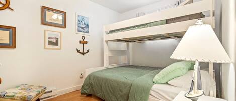 A bunk bed room with a ceiling fan, framed pictures on the wall, and a bedside lamp.