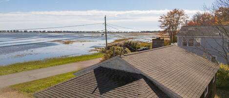 A house with a sloped roof, a visible chimney, and a paved pathway leading to a body of water.