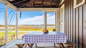 A covered outdoor seating area with a checkered table and bench, overlooking a field. - Salt Box by the Sea: Water View - Charming 3-bedroom Cottage in Wells! (Wells)