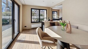 A modern dining area with a large table, chairs, and a view through large windows.