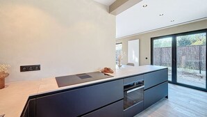 A modern kitchen with a large island, built-in oven, and a sliding glass door to the outdoors.