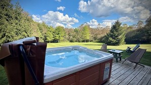Ein Whirlpool auf einer Holzterrasse mit einem Rasen und Bäumen im Hintergrund.