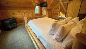 Ein Schlafzimmer einer Holzhütte mit einem Bett, einem Deckenventilator, einem Fernseher und einem Kamin.