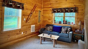 Ein Holzblockhaus-Innenraum mit einer Couch, einem Couchtisch und zwei mit Vorhängen versehenen Fenstern.