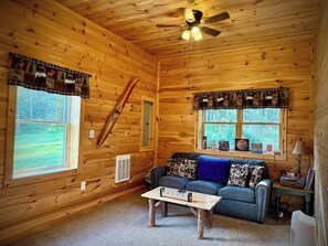 L’intérieur d’une cabane en rondins, avec un canapé, une table basse et deux fenêtres dotées de rideaux.