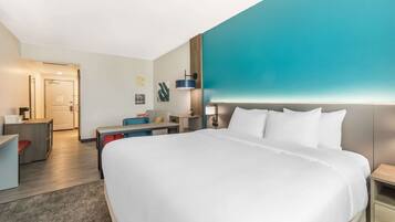 A modern hotel room with a large bed, a desk, a chair, and a nightstand.