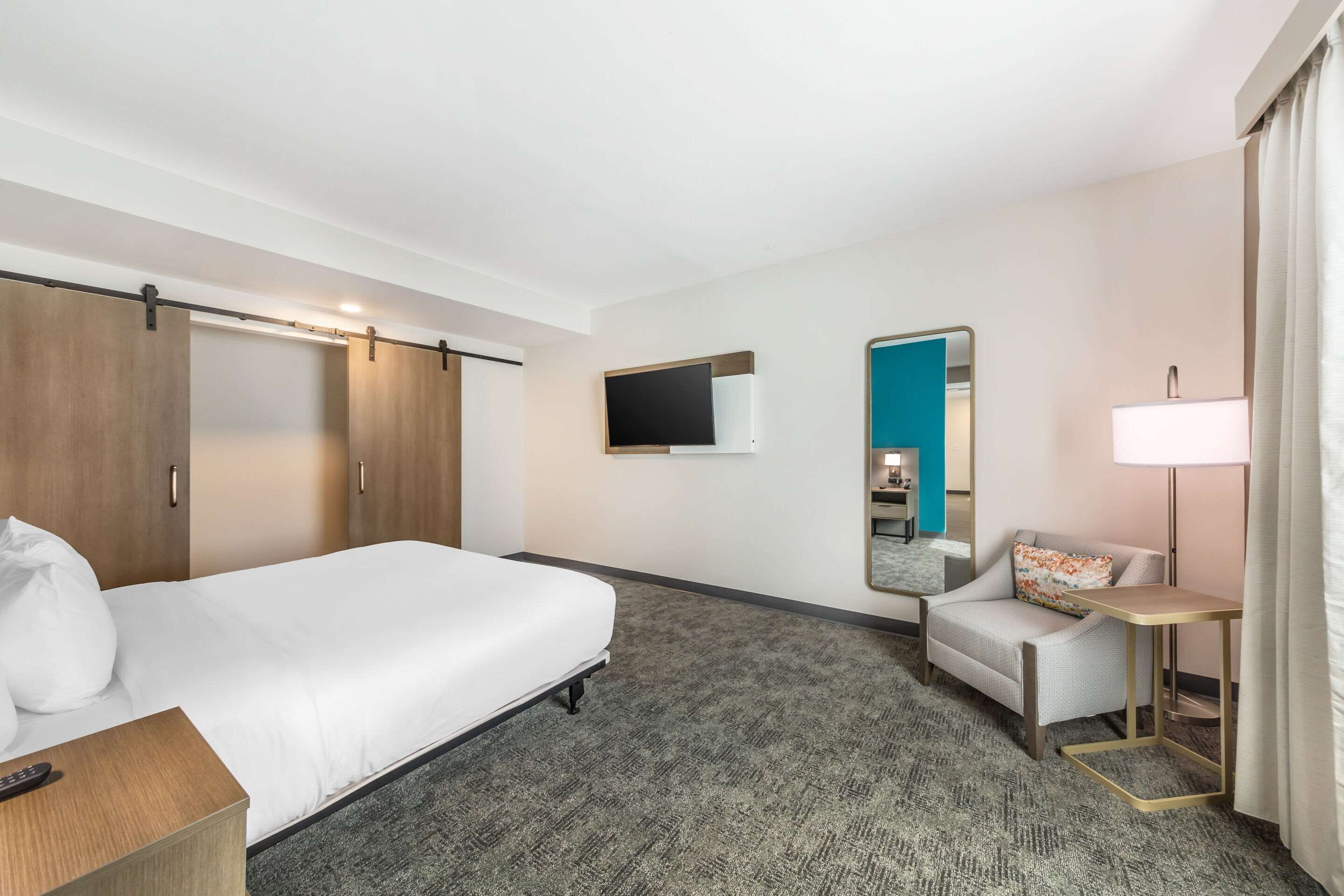 A hotel room with a bed, a desk, a chair, a TV, and a mirror.