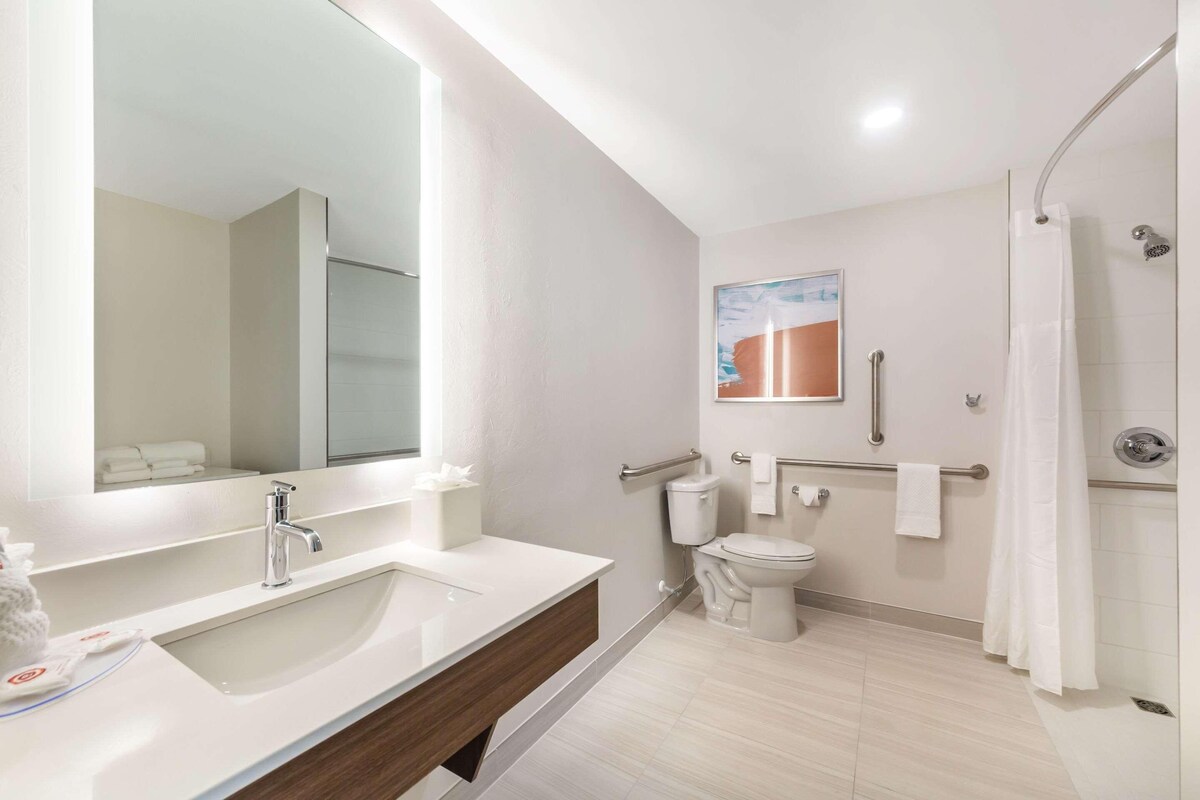 A modern bathroom with a large mirror, a sink, a toilet, and a shower area.