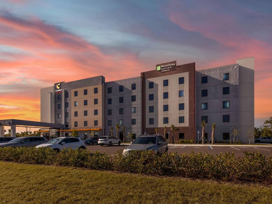 A hotel with multiple floors, a parking lot, and a sunset sky.