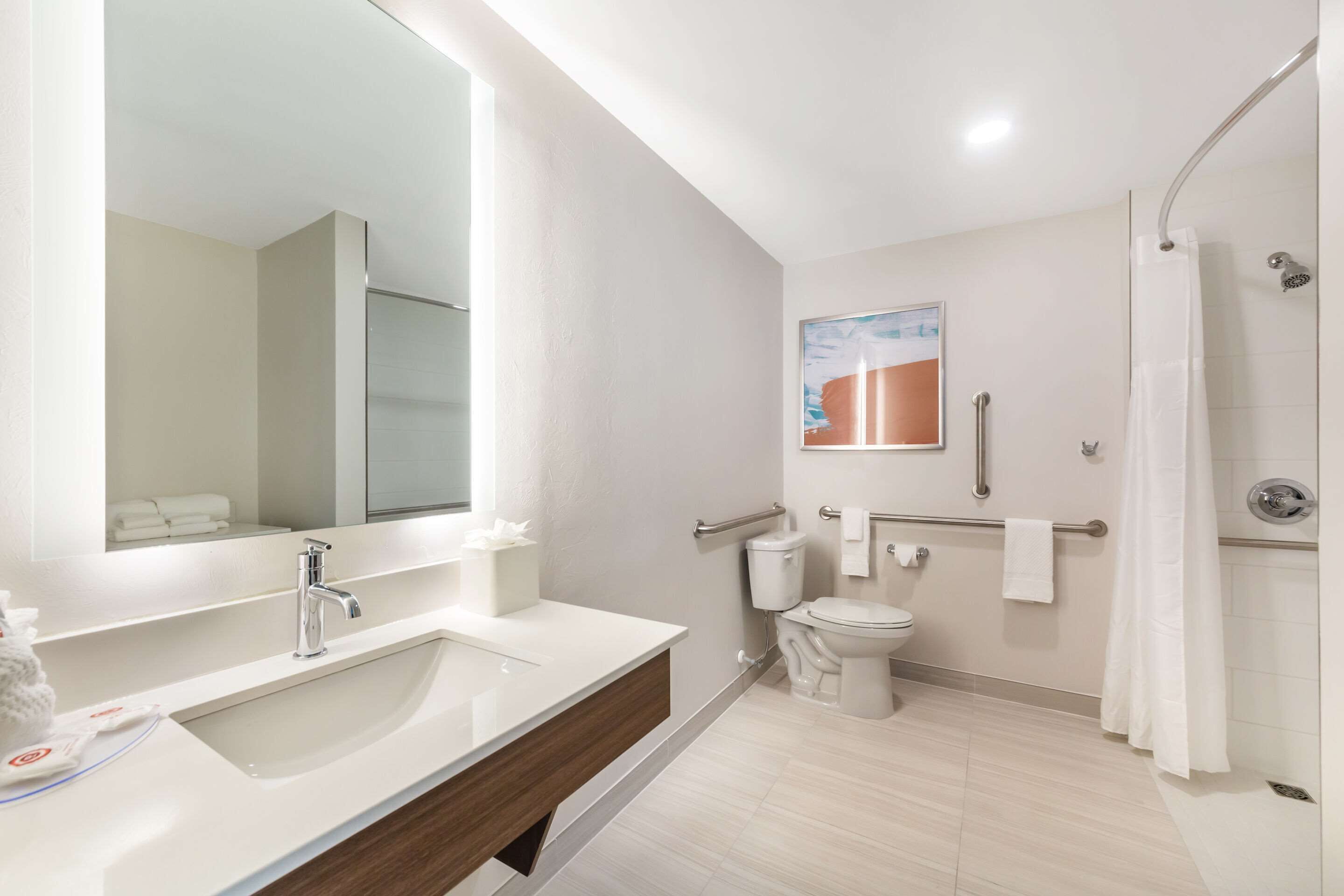 A modern bathroom with a large mirror, a sink, a toilet, and a shower.