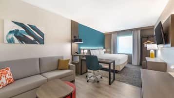 A modern hotel room with a bed, a desk, a sofa, a chair, and a TV.