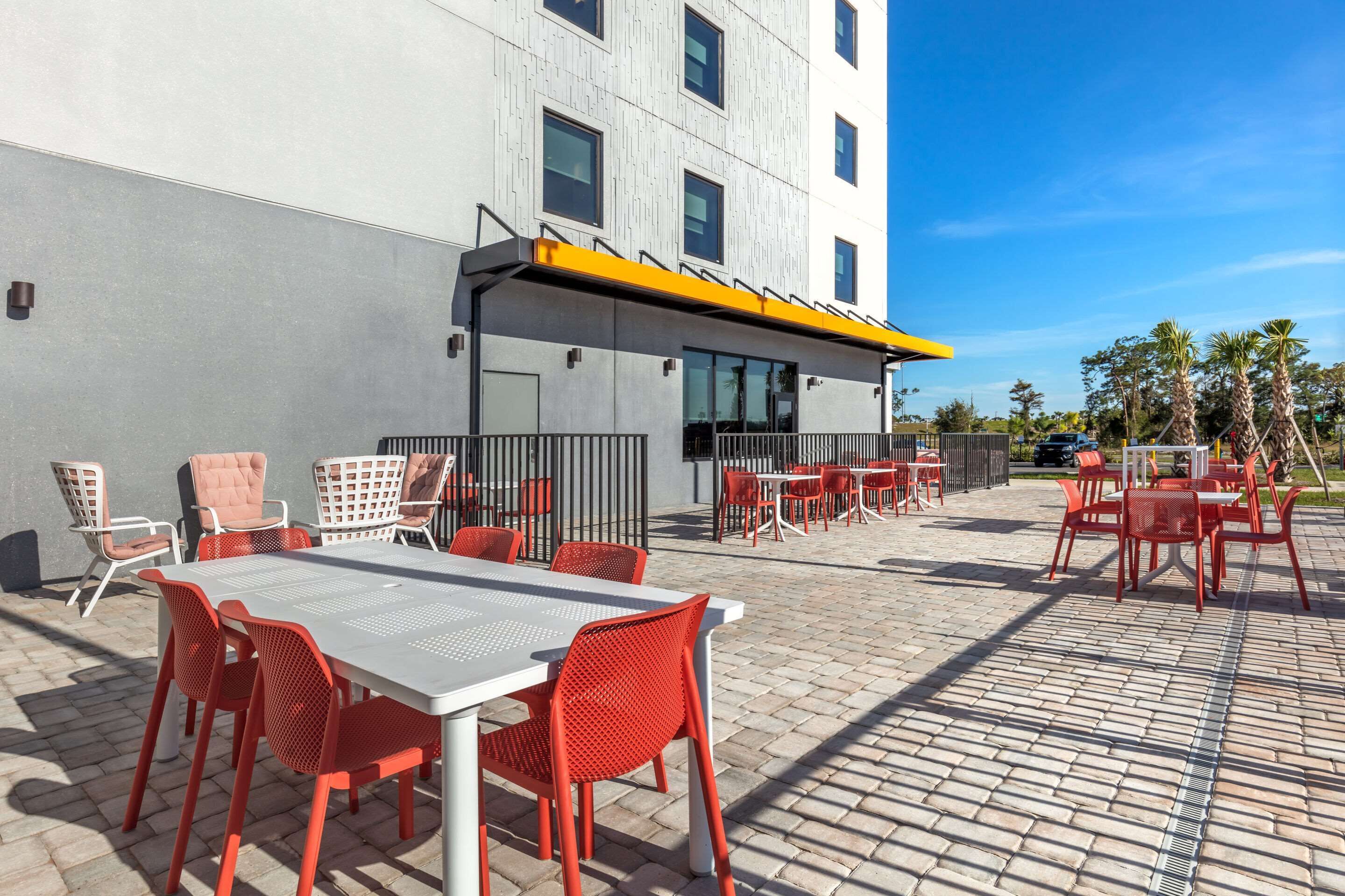 An outdoor patio with tables and chairs, a covered seating area, and a building in the background.