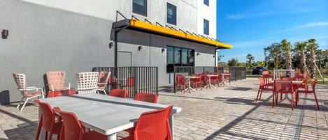 An outdoor patio with tables and chairs, a covered seating area, and a building in the background.