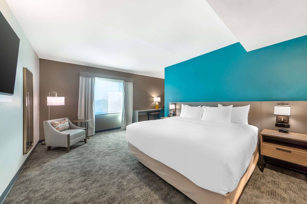 A hotel room with a large bed, a desk, a chair, and a view of the outdoors.