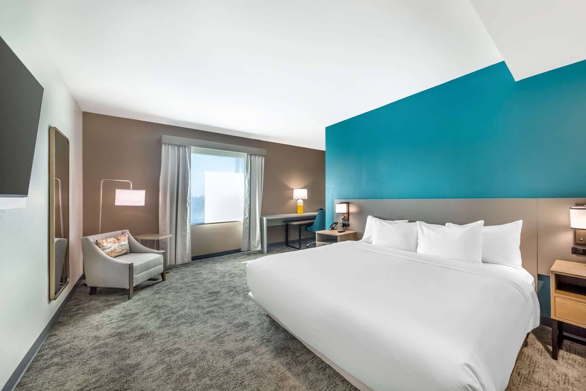A hotel room with a large bed, a desk, a chair, and a window with curtains.