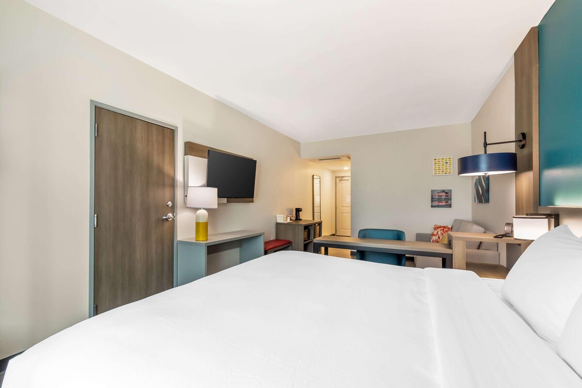 A hotel room with a bed, a desk, a chair, a television, and a lamp.